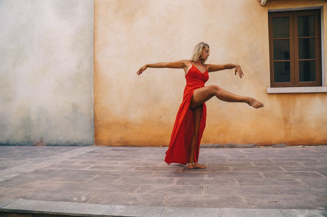 Una bailarina con vestido rojo en plena pose ante un muro de terracota iluminado por el sol